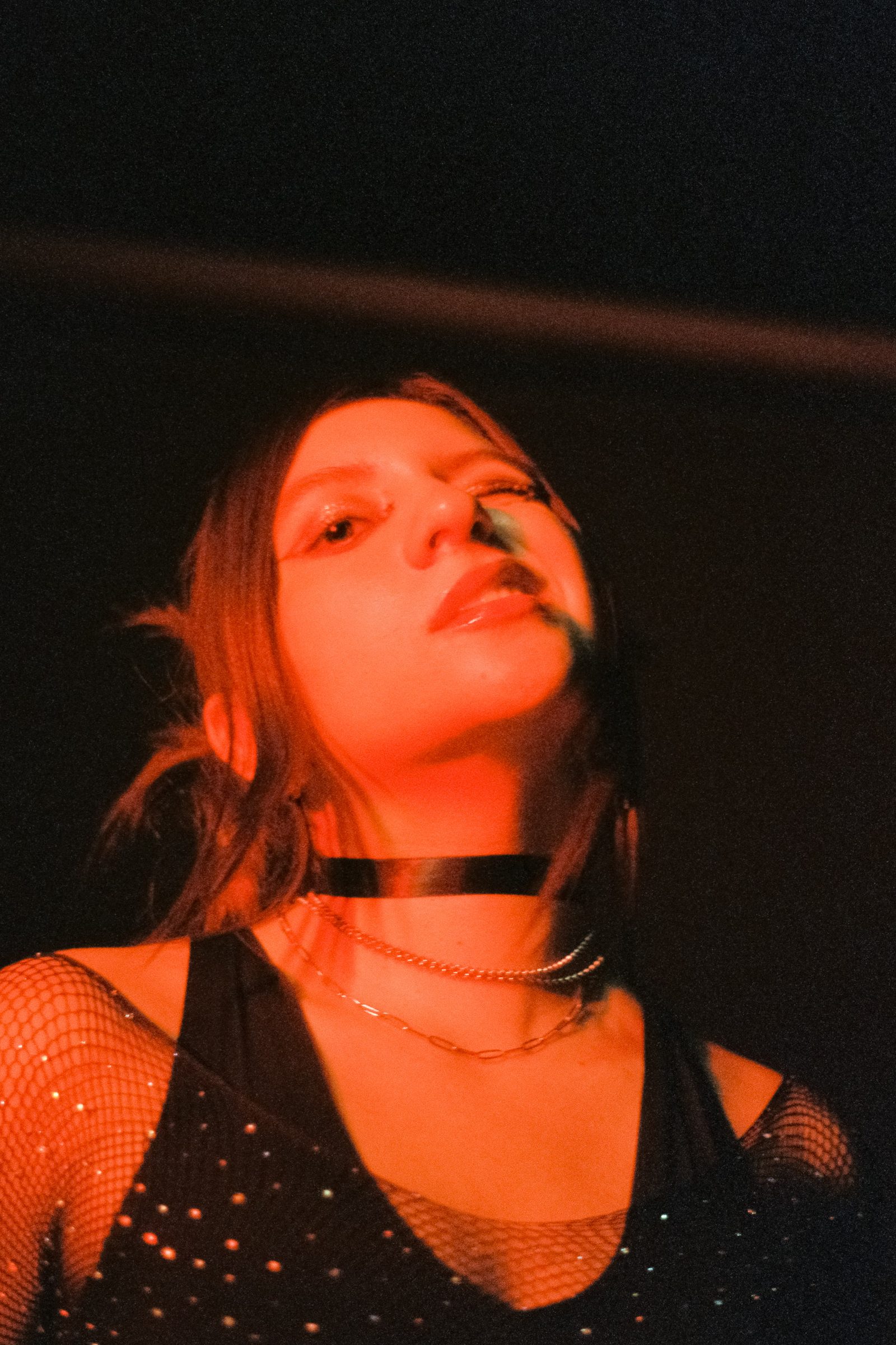 Close-up portrait of Angela Hernandez in red nighttime light, with dark shadows and a punk-inspired black outfit.