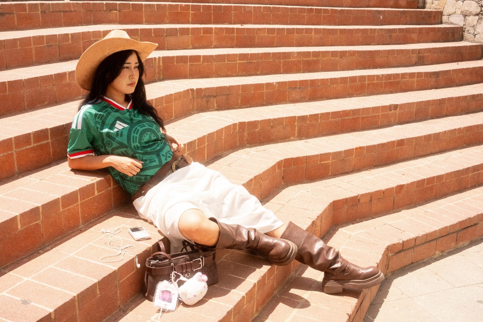 Liz con sombrero y el jersey de la Selección Mexicana recostada en unas escaleras de ladrillo
