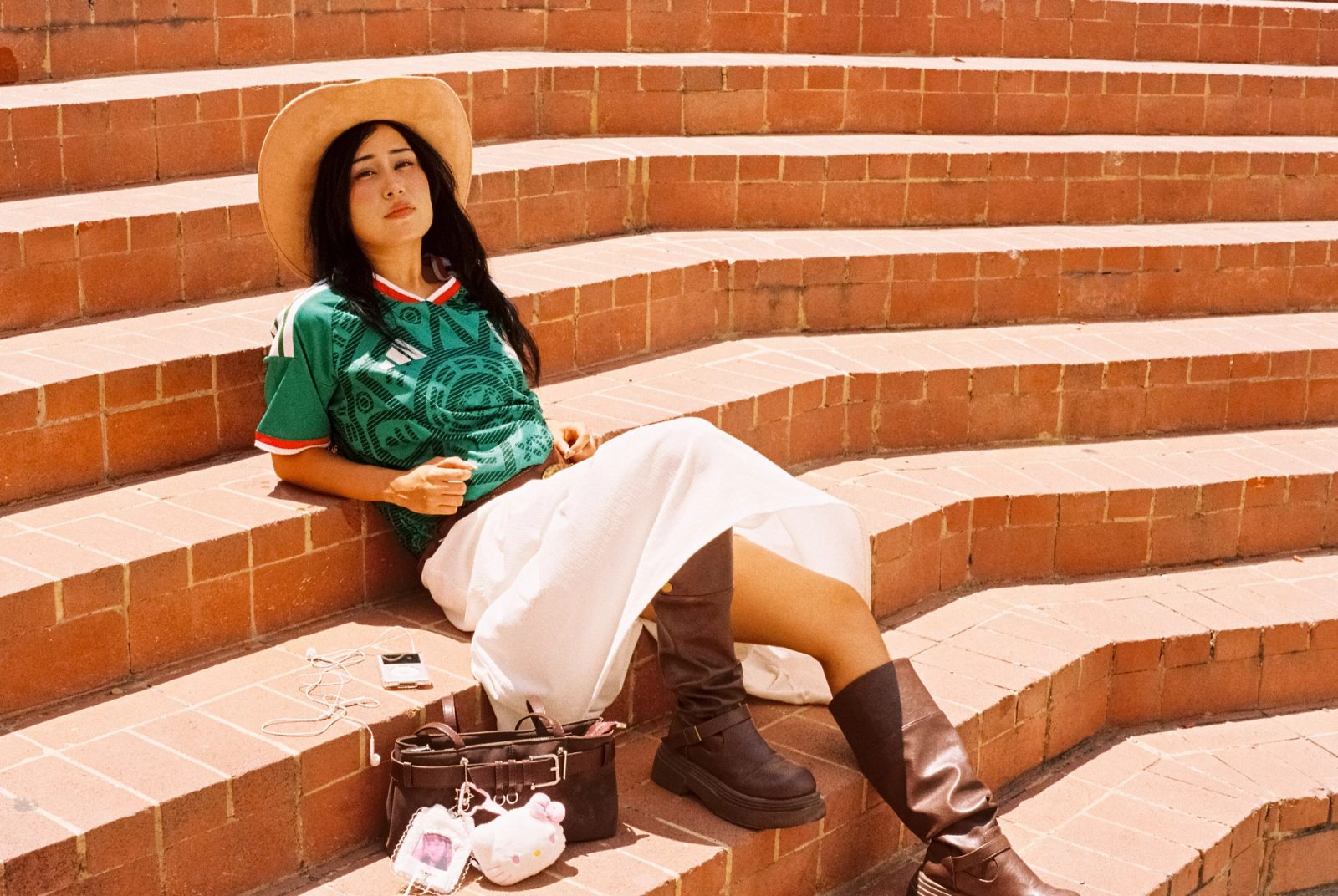 Liz con sombrero y el jersey de la Selección Mexicana recostada en unas escaleras de ladrillo