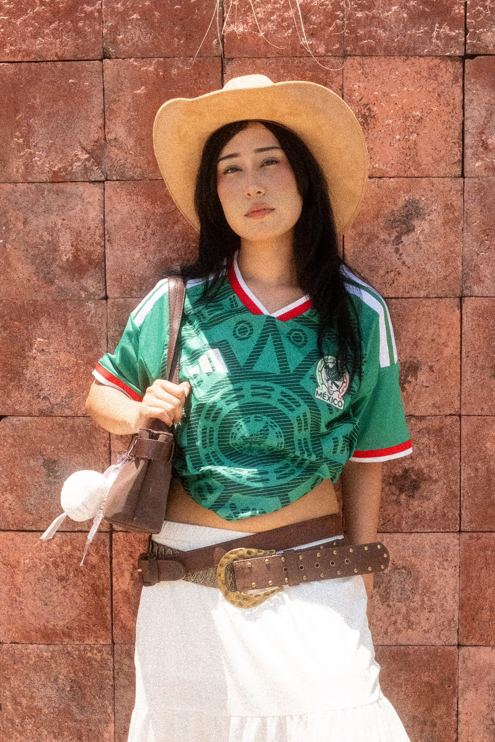 Liz con sombrero y el jersey de la Selección Mexicana en un fondo de losetas de adobe