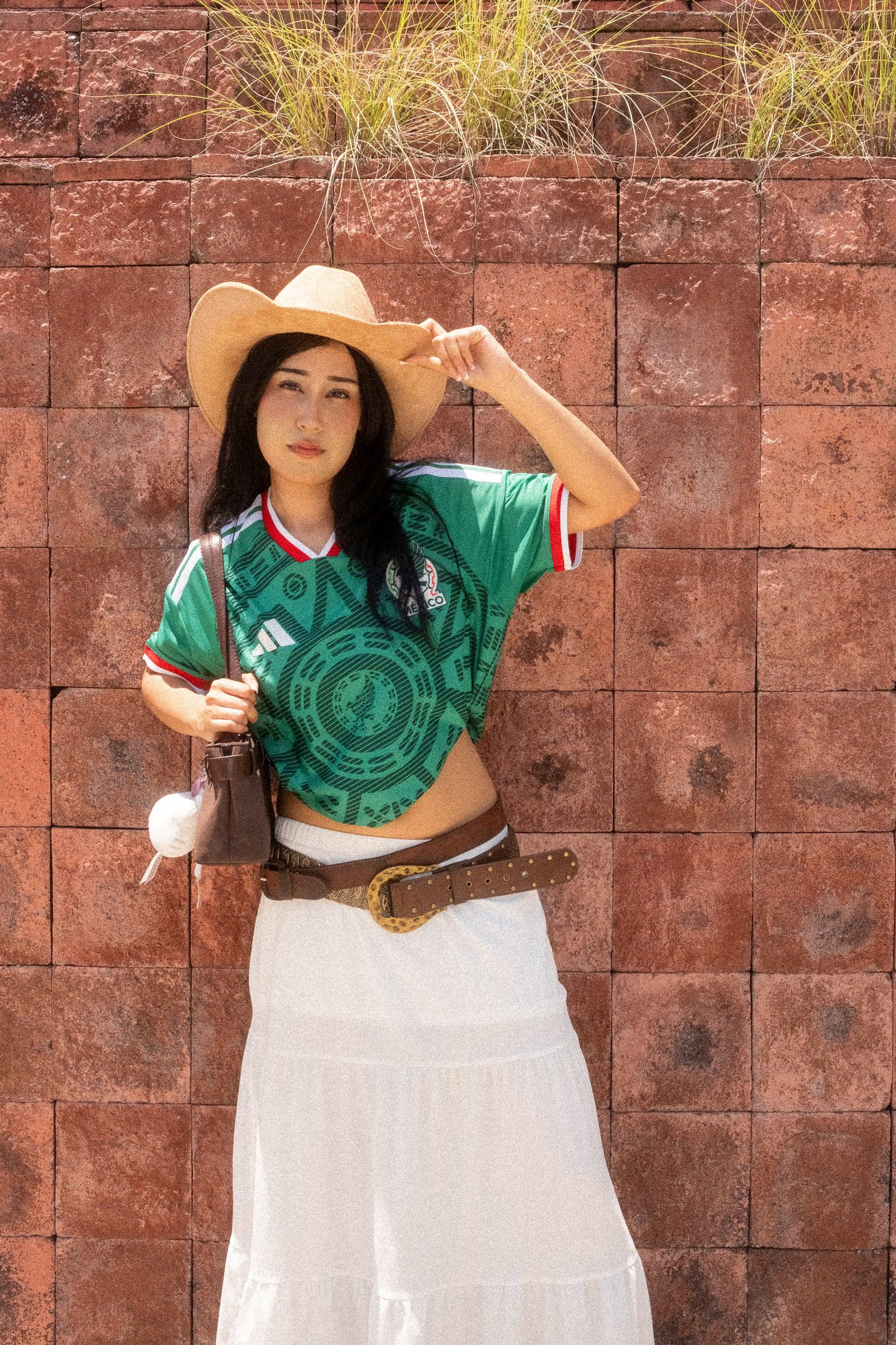 Liz con sombrero y el jersey de la Selección Mexicana en un fondo de losetas de adobe