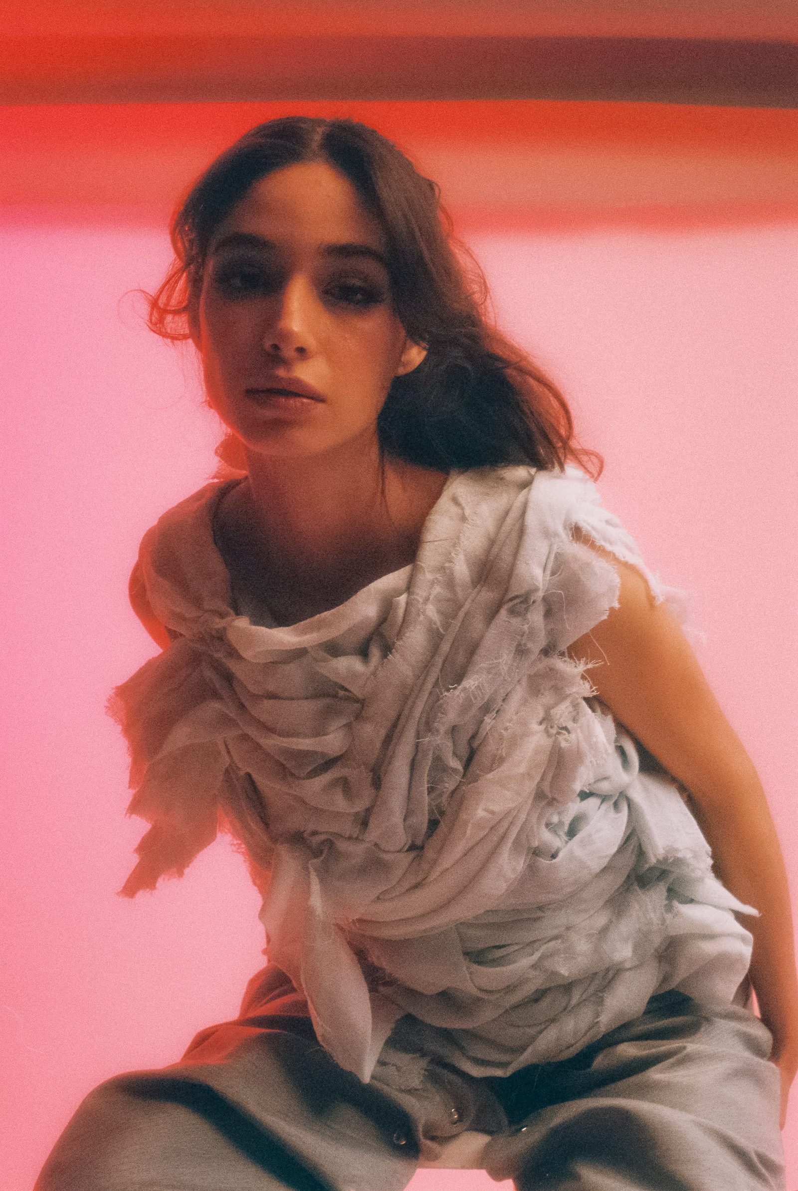 Michelle Malacara in a sculptural pale fabric top and gray pants, photographed on film in a studio with soft pink light.