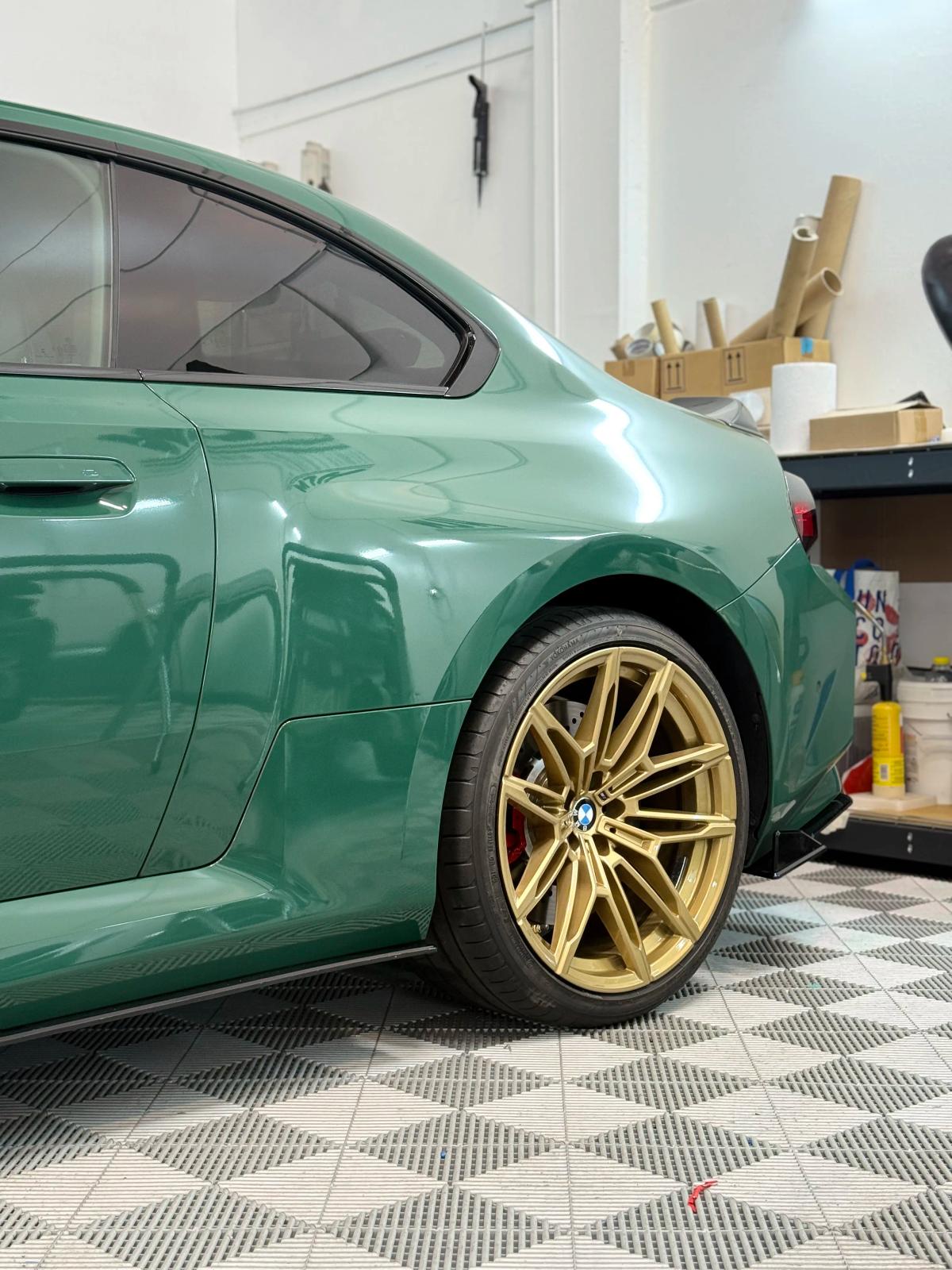 Aleta trasera ensanchada y llanta dorada de un BMW M2 deportivo en aboutwrap garage.