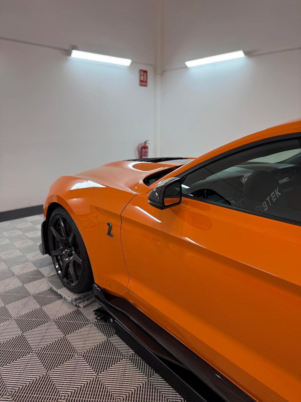  Perfil delantero de un Ford Mustang Shelby de color naranja en el taller de aboutwrap garage.