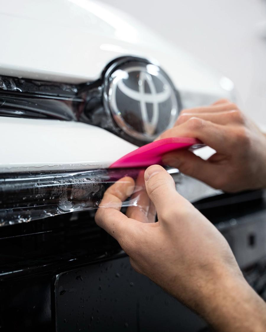 Aplicación de Paint Protection Film (PPF) con espátula en el parachoques delantero de un coche en aboutwrap garage.
