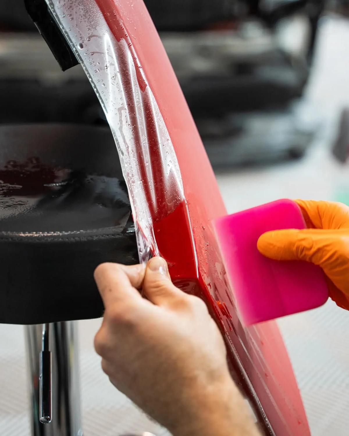 Aplicación de PPF sobre la carrocería de color rojo brillante con espátula rosa en aboutwrap garage.