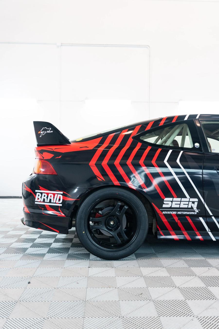 Lateral de un coche de competición negro con gráficas geométricas en rojo y blanco en aboutwrap garage.