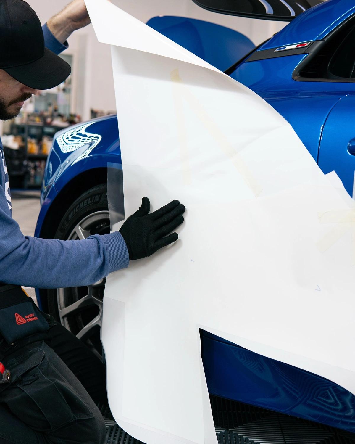  Técnico aplicando una plantilla de gran formato en el lateral de un coche deportivo azul en aboutwrap.