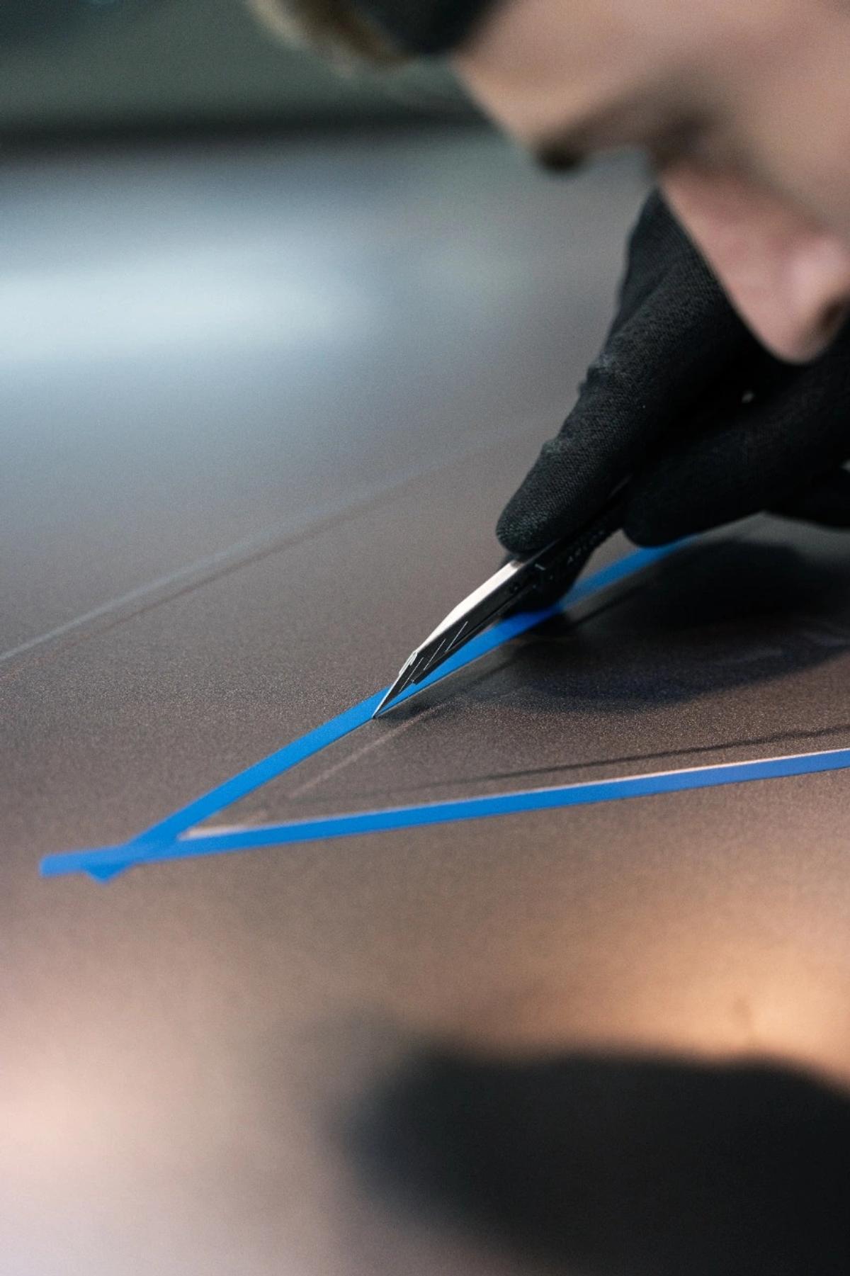 Primer plano del corte de precisión con cinta de enmascarar azul sobre panel vinilado.