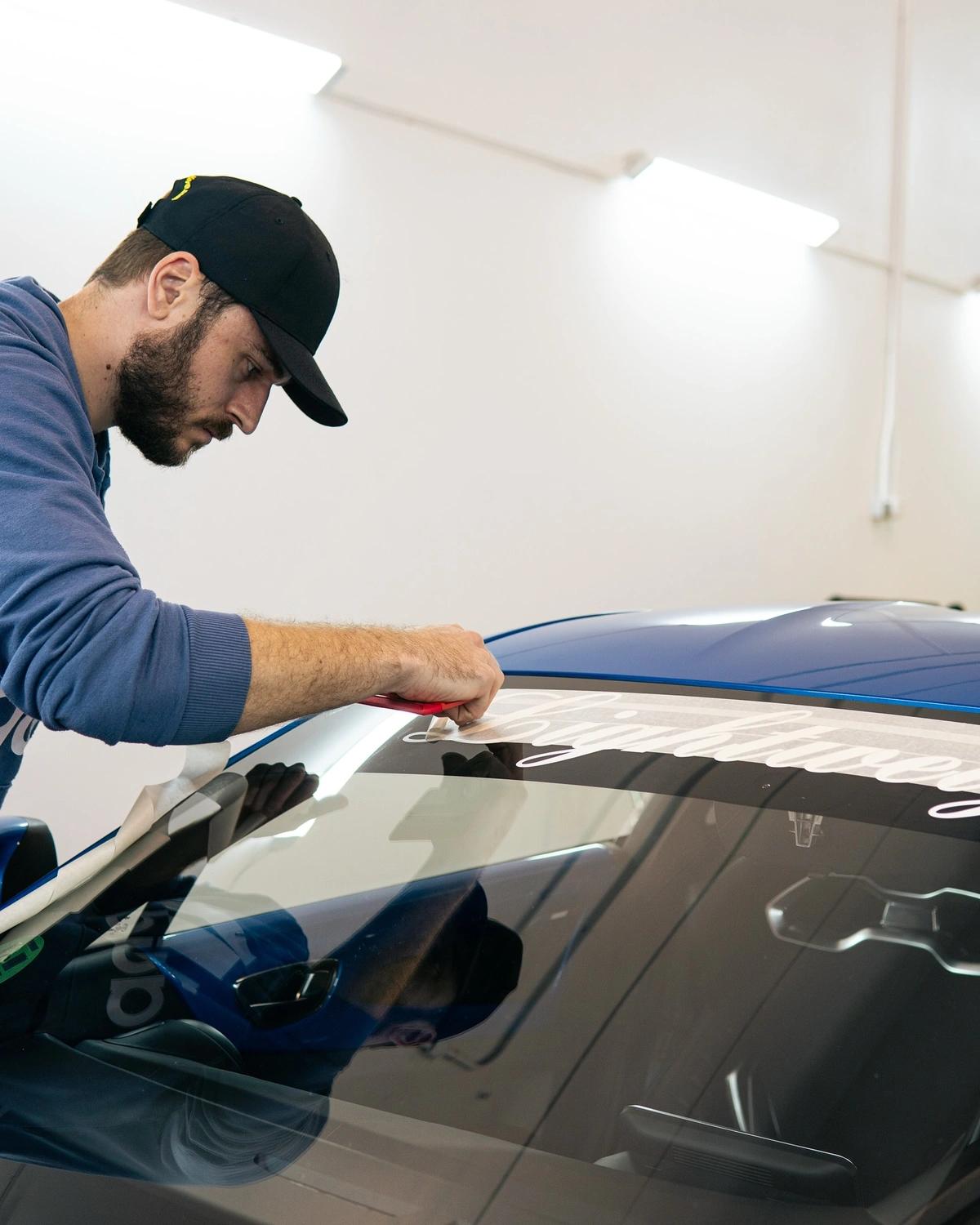 Especialista instalando un vinilo decorativo en la parte superior del parabrisas de un coche en aboutwrap.