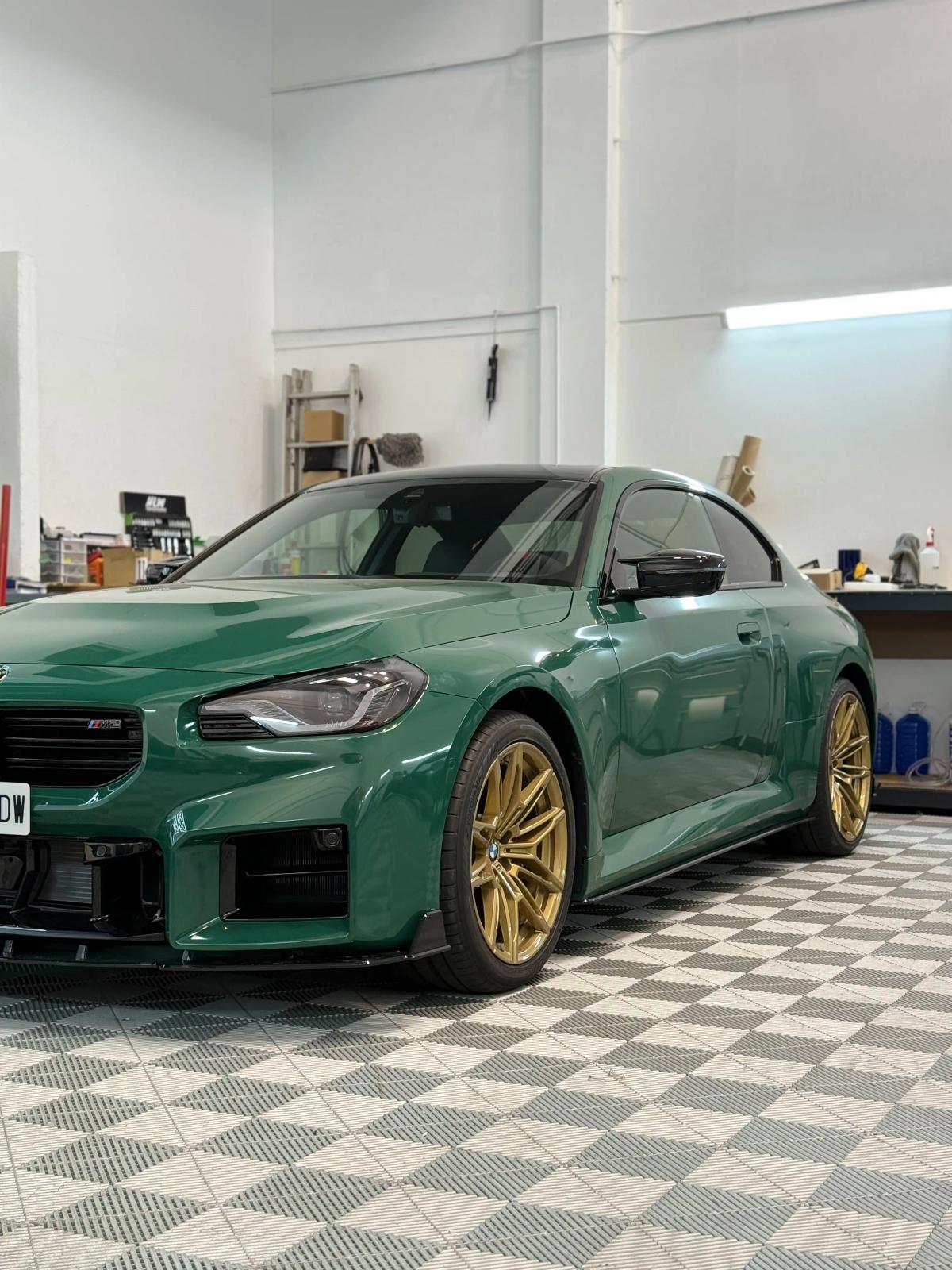 Vista frontal de un BMW M2 en color verde británico con llantas doradas en el estudio de aboutwrap garage.