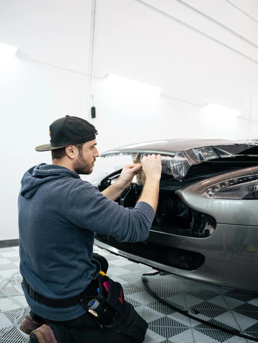 Técnico de aboutwrap garage instalando vinilo protector en la zona superior del frontal de un coche de lujo.