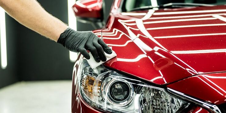 Gloved hand wiping a red car headlight