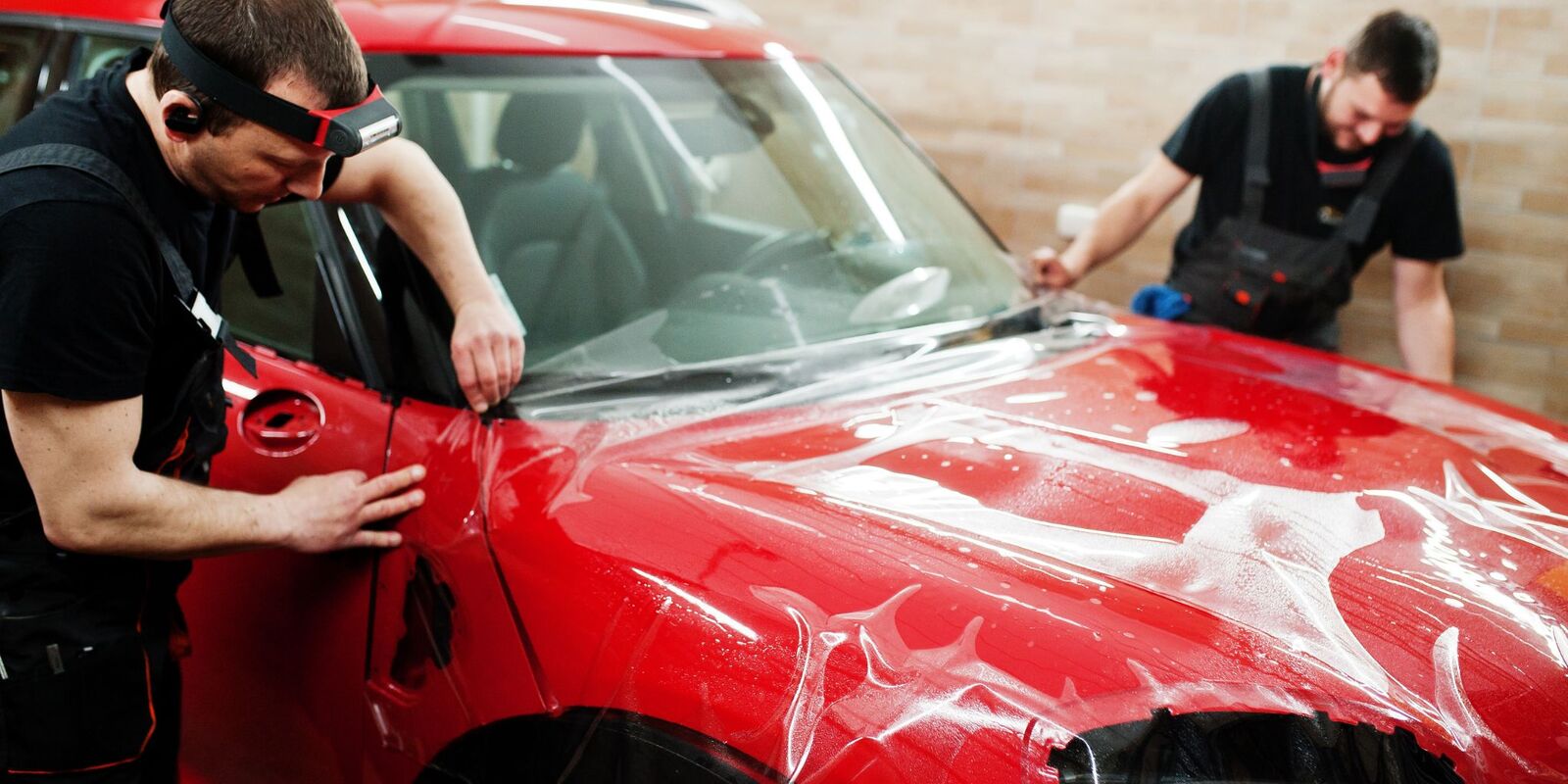 Two technicians applying protective film to a red car hood