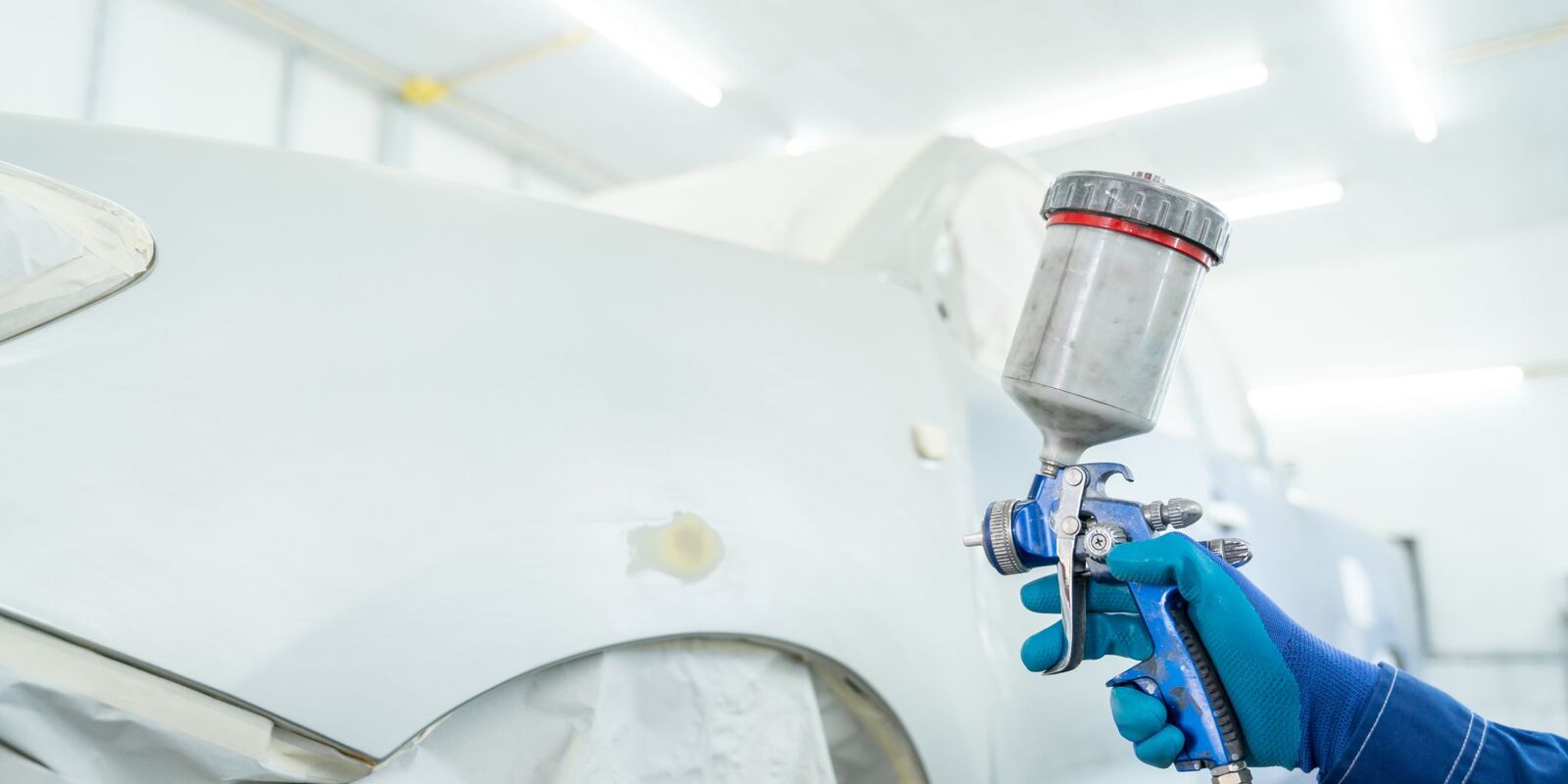 Spray gun painting a white car panel