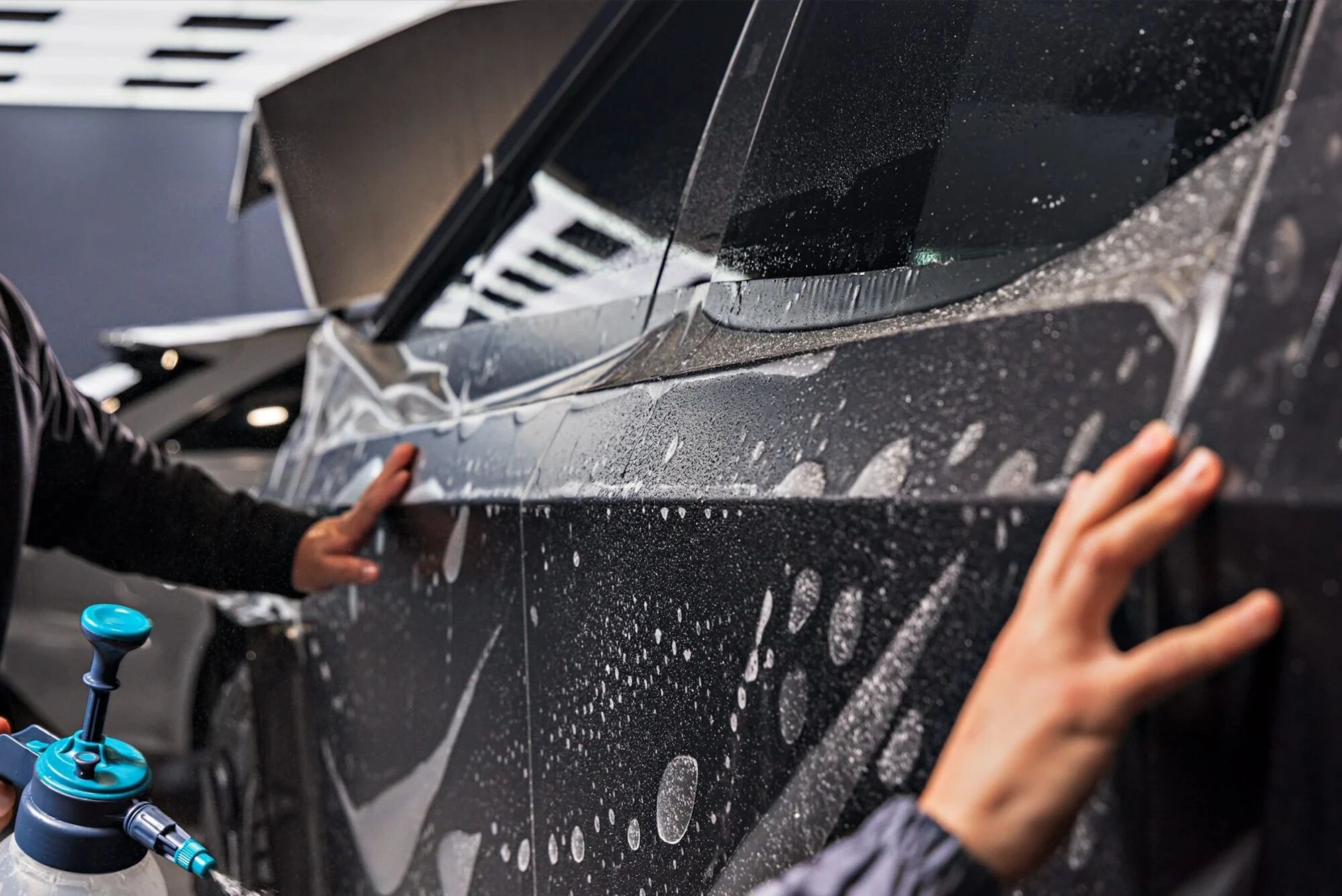 Hands smoothing paint protection film onto a wet car door