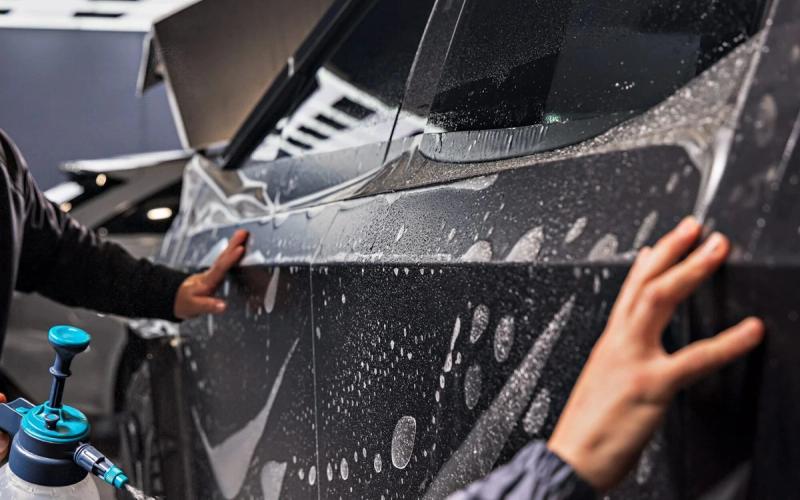 Hands smoothing paint protection film onto a wet car door