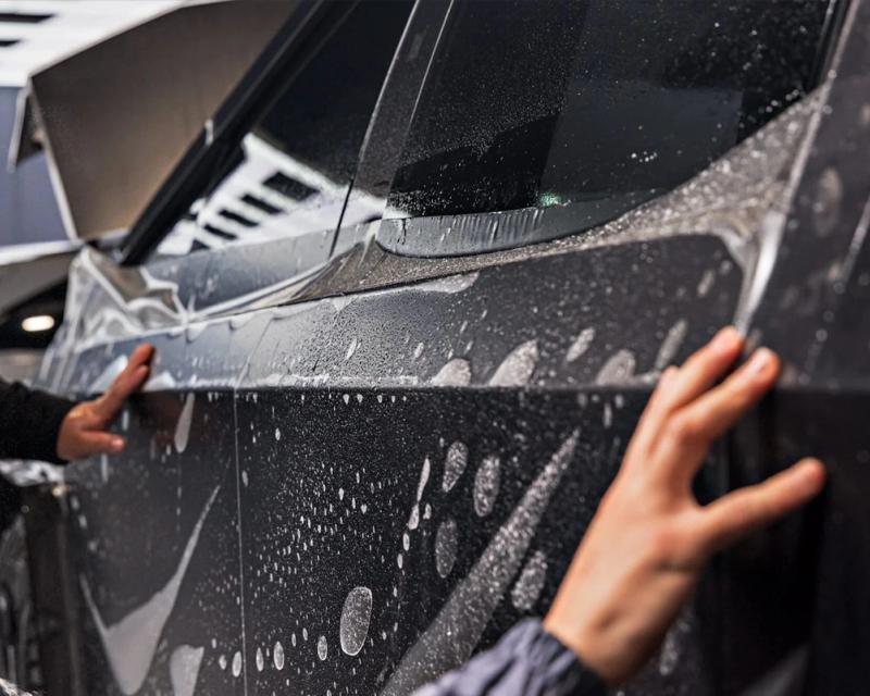 Hands smoothing paint protection film onto a wet car door