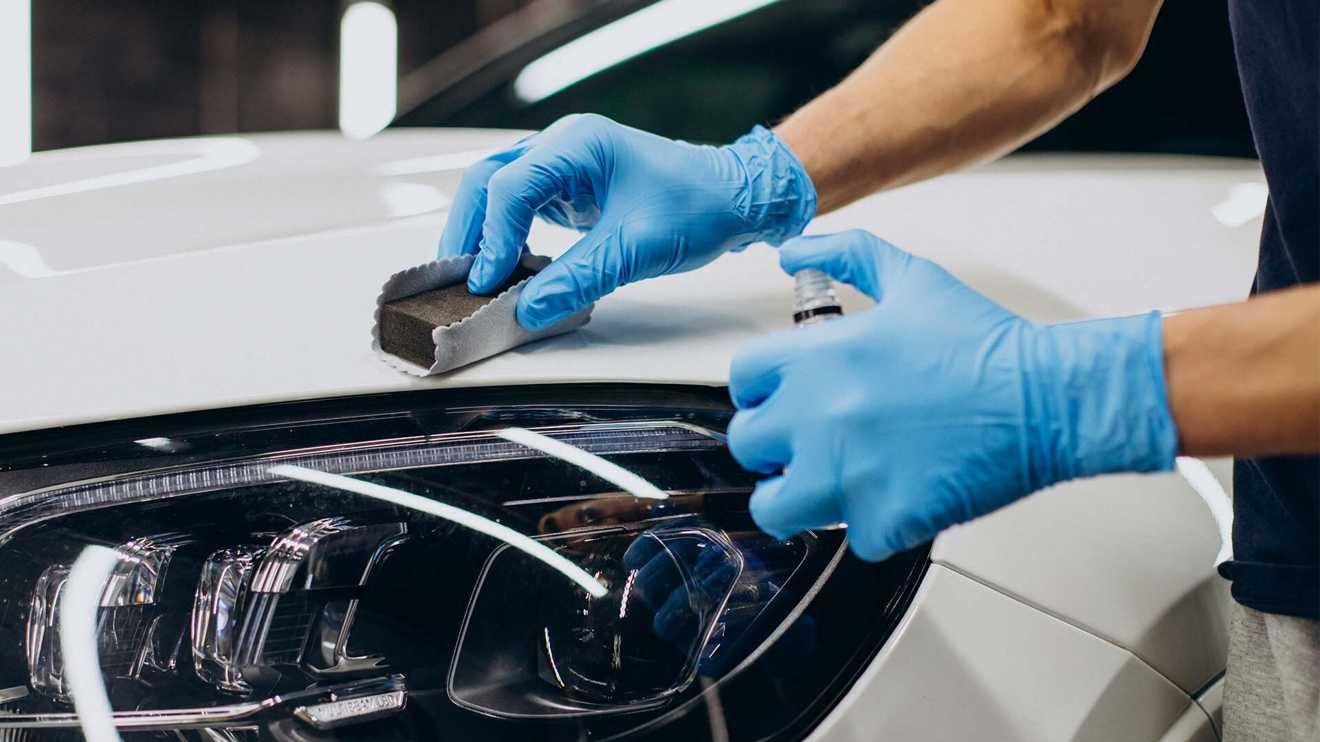 Gloved hand applying ceramic coating beside a headlight on a white car
