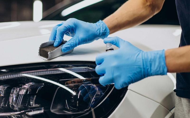 Gloved hand applying ceramic coating beside a headlight on a white car