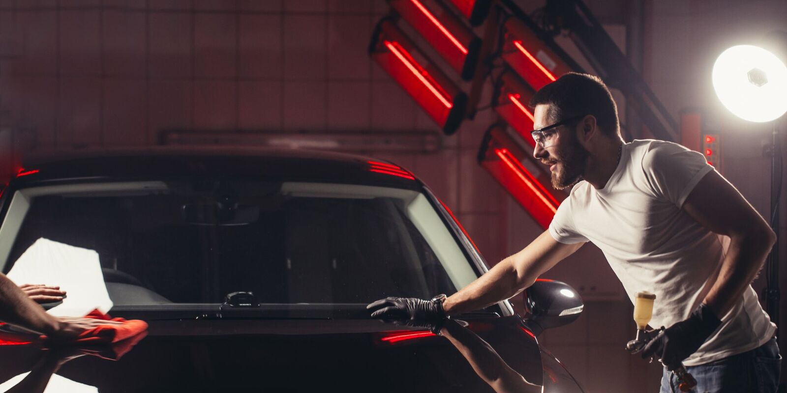 Man wiping a black car under red booth lights