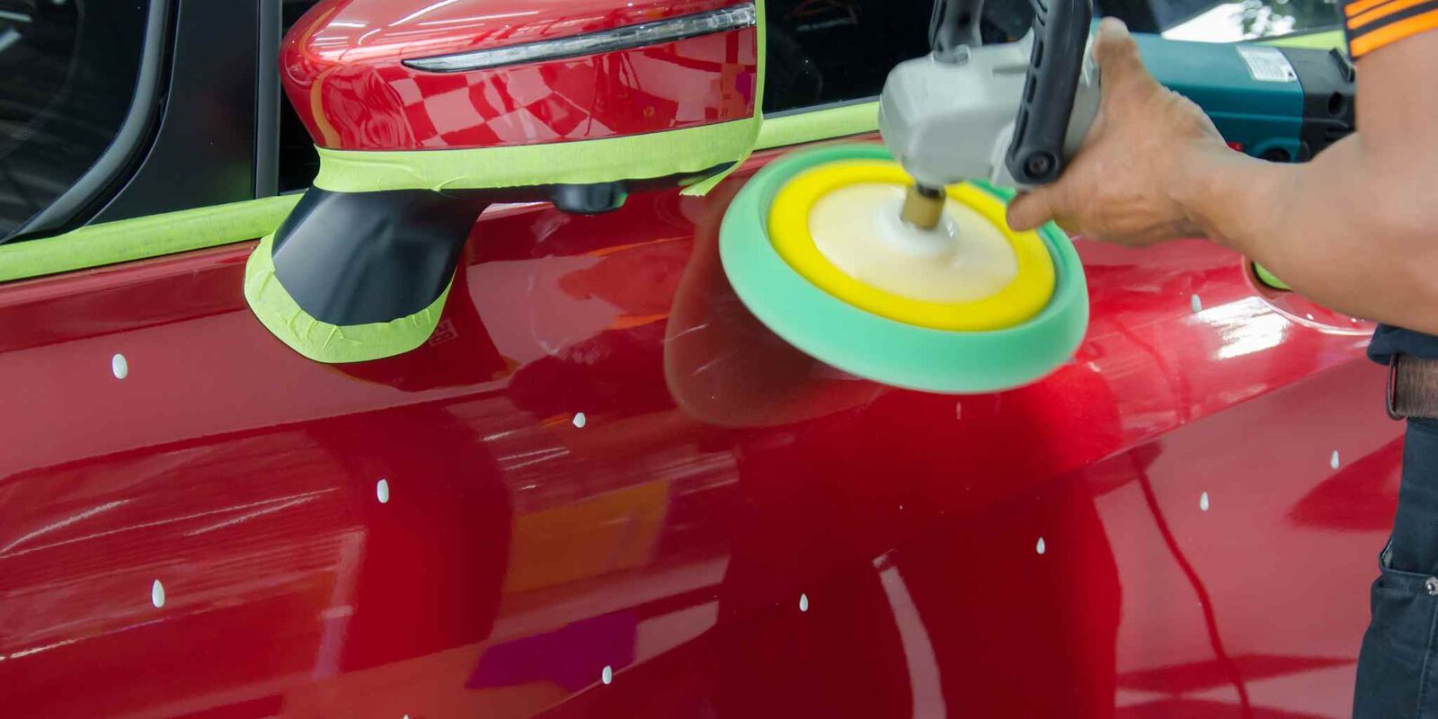 Polisher with a yellow pad working a red car panel
