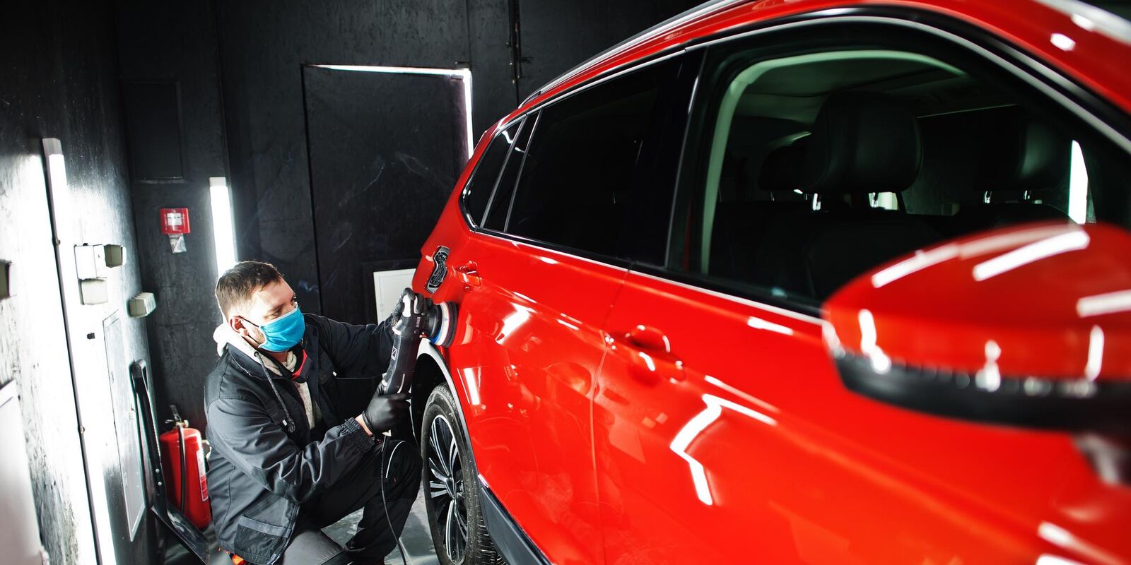 Technician polishing a red car in a paint booth