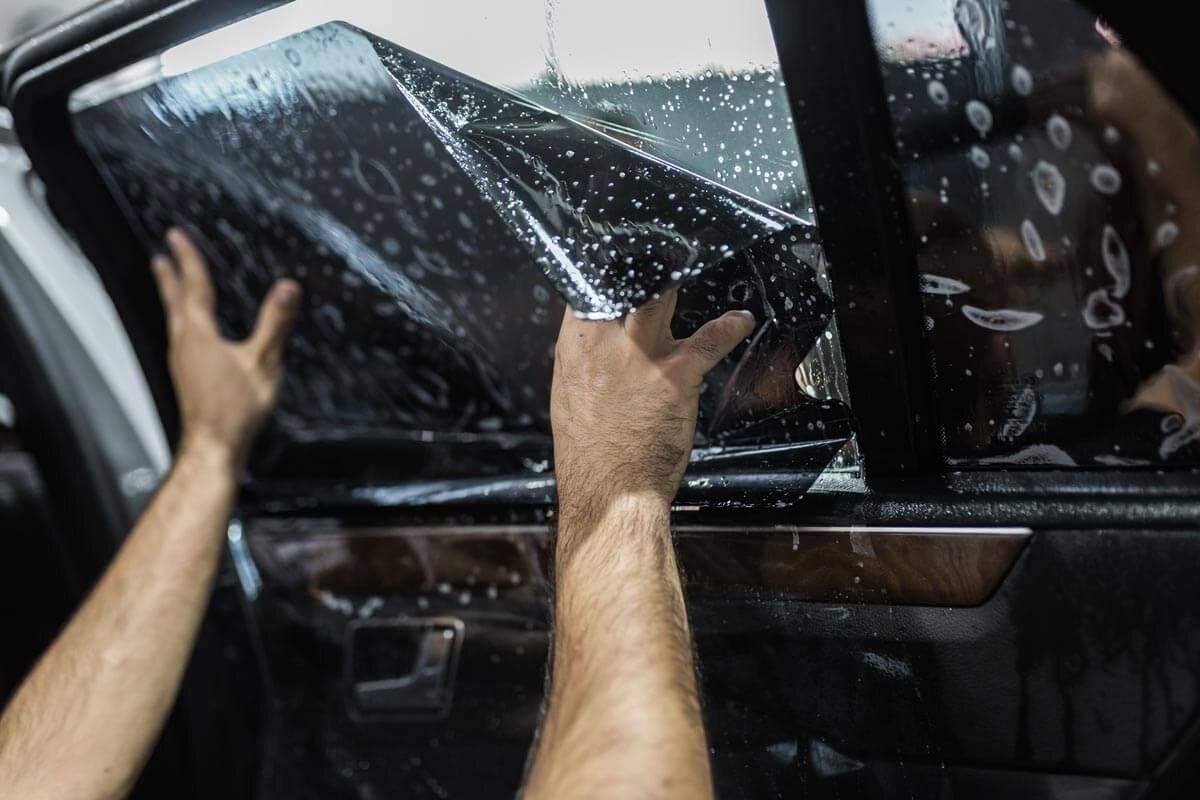 Hands positioning wet window tint film on the inside of a car door window