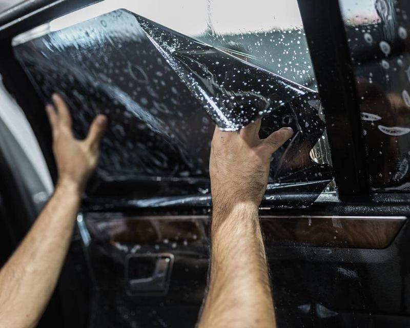 Hands positioning wet window tint film on the inside of a car door window