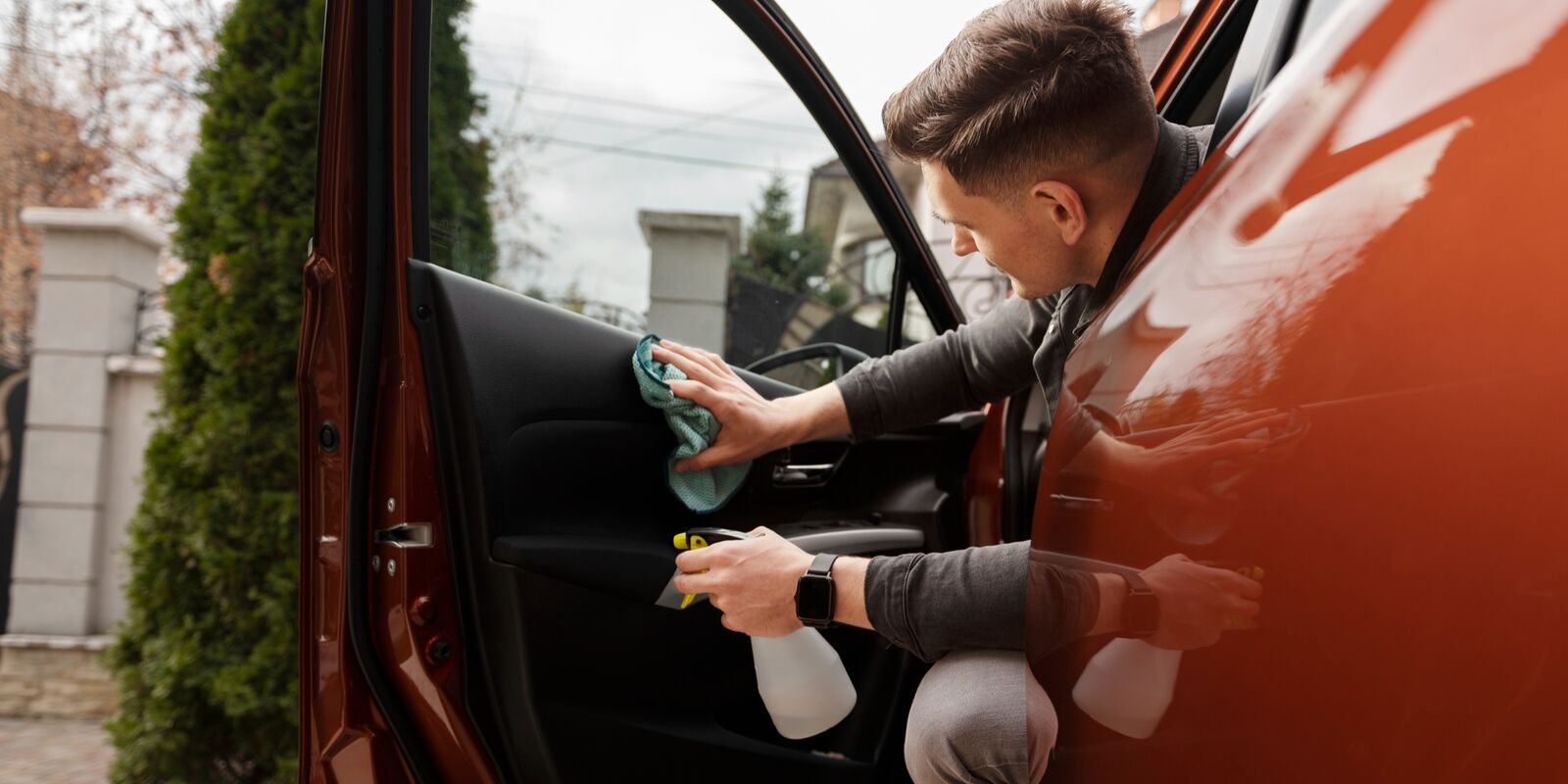 Man wiping the door panel of a red car with the door open
