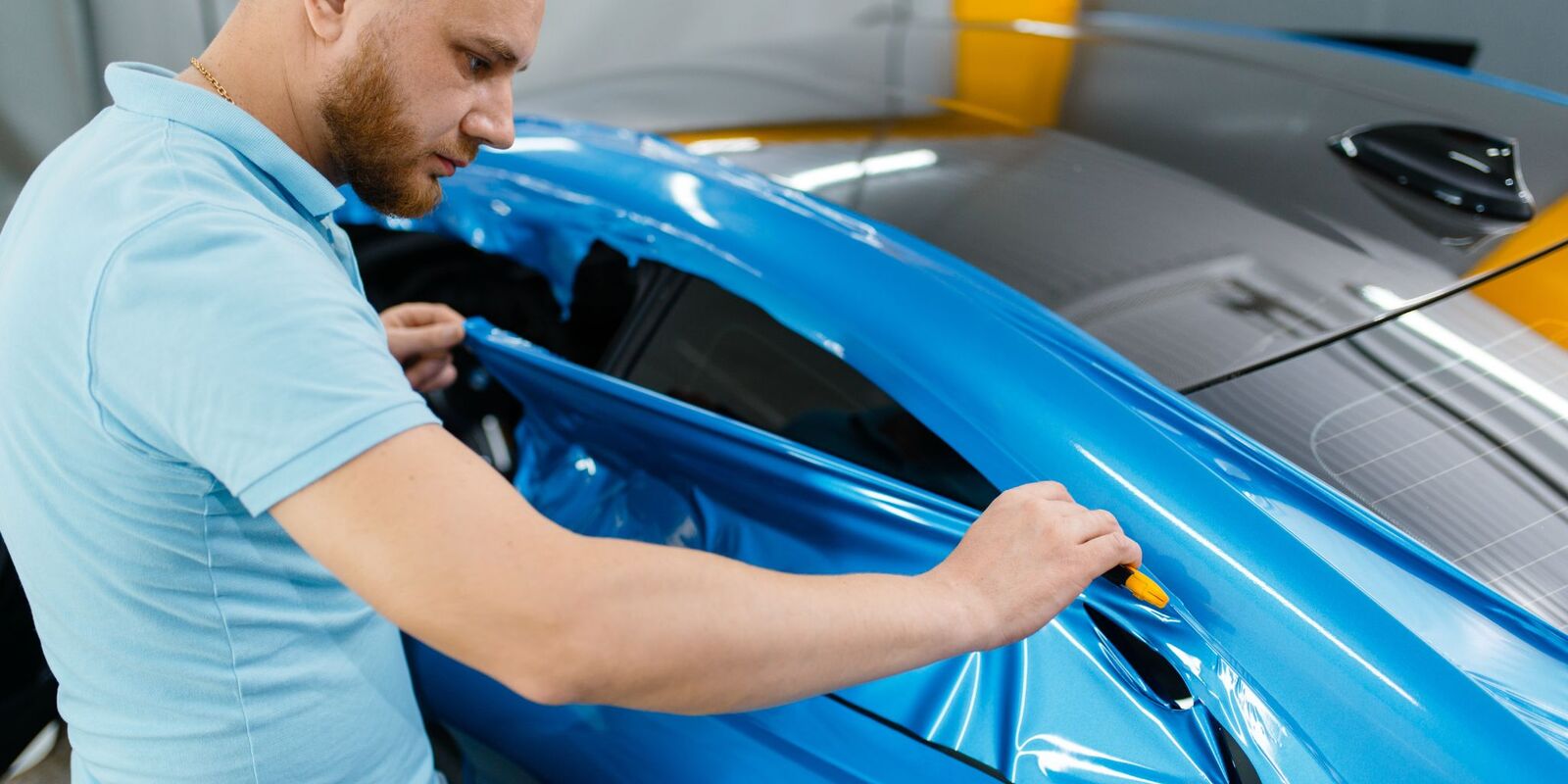 Man applying blue vinyl wrap to a car