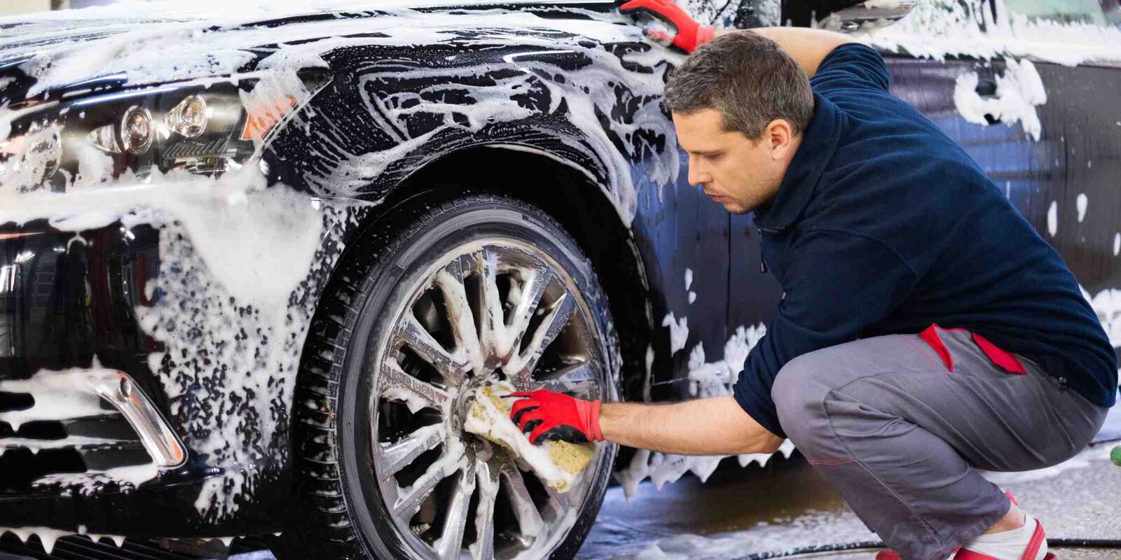 Man scrubbing a wheel on a foam-covered car