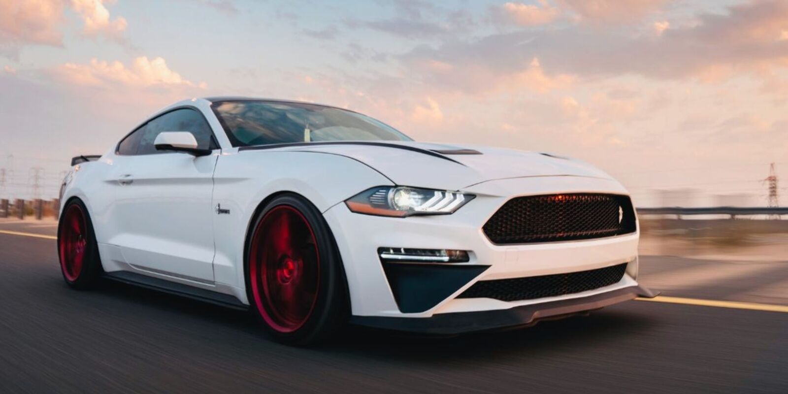 White Mustang driving on a road at sunset