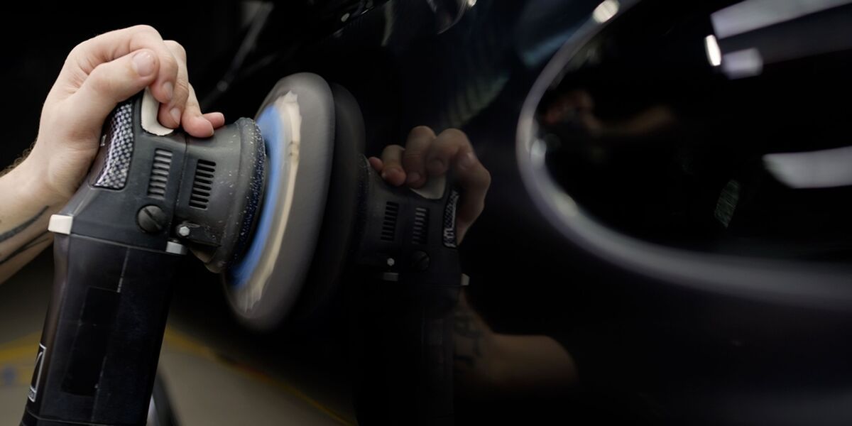 Dual-action polisher on dark paint inside a detailing bay