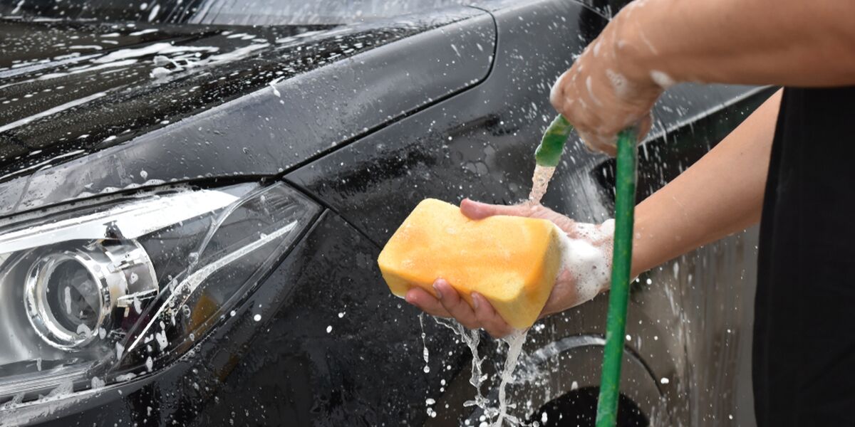 Hand washing a black car with a yellow sponge