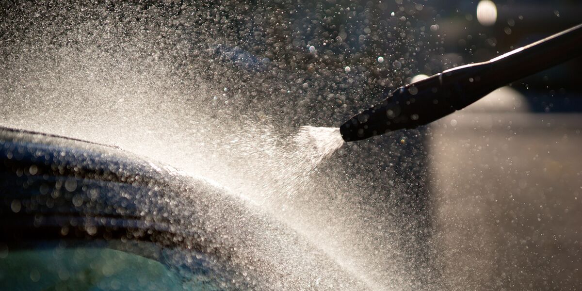 High-pressure water spray across a dark car surface
