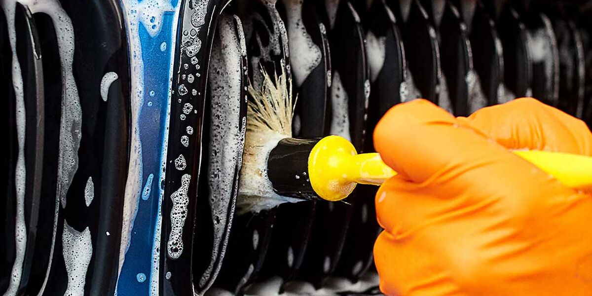 Gloved hand brushing a foam-covered blue car grille