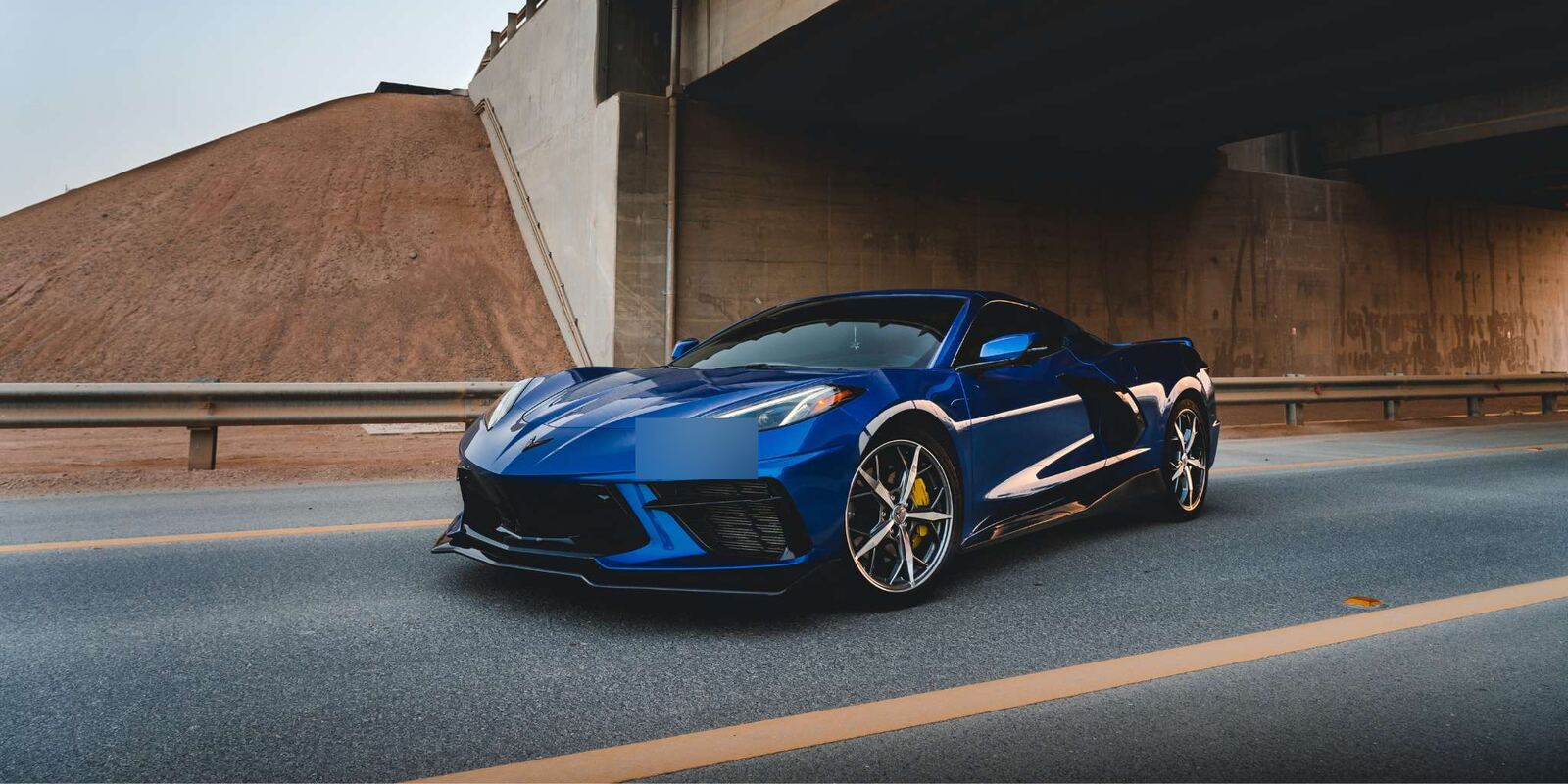 Blue Corvette on a road beneath an overpass