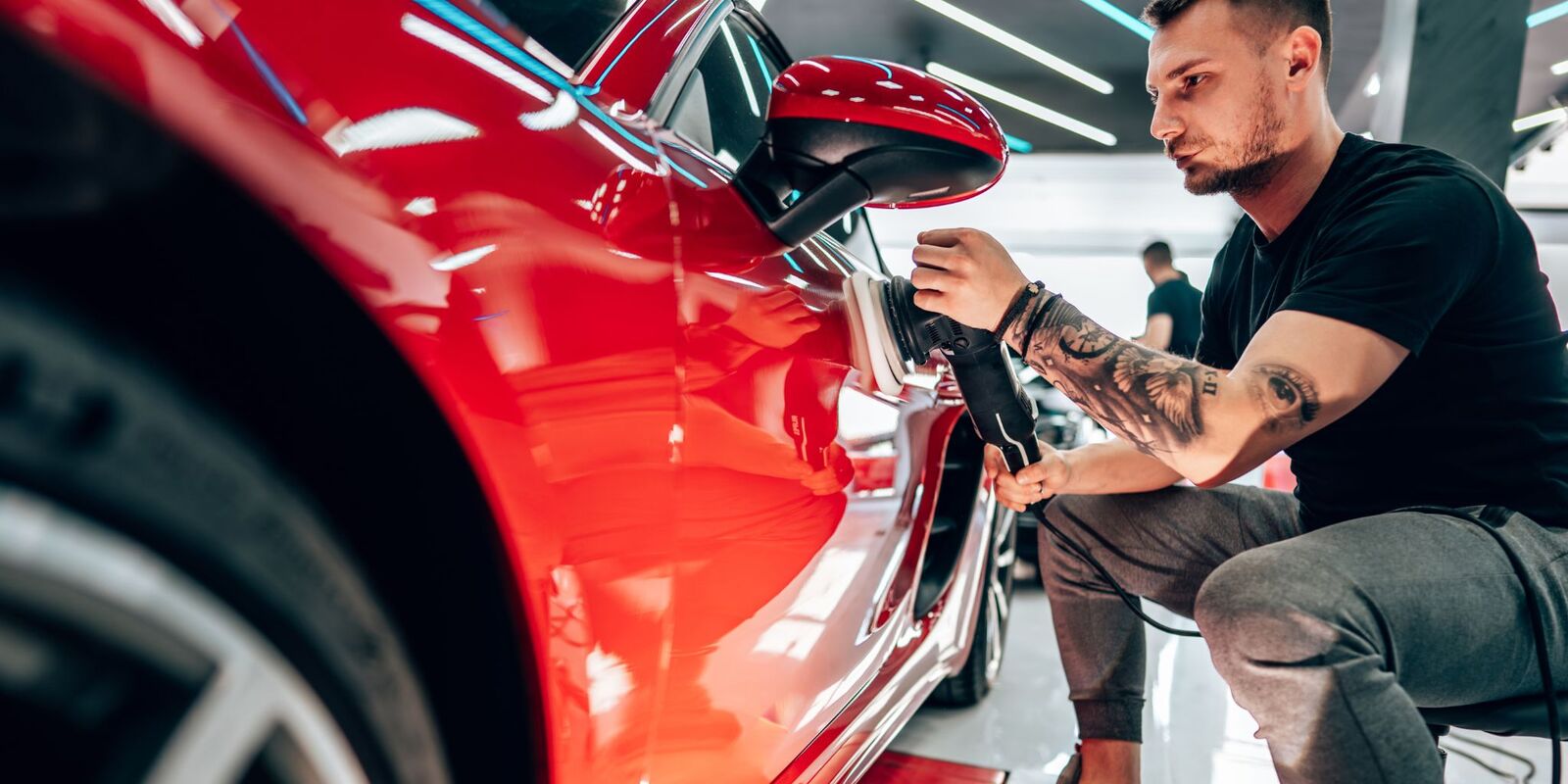 Man with tattoos wiping a red car door