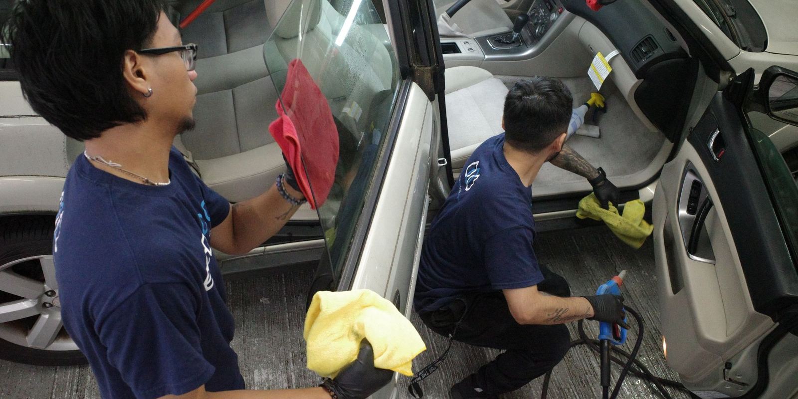 Two Eco Car Cafe technicians in navy shirts cleaning the interior of a white SUV