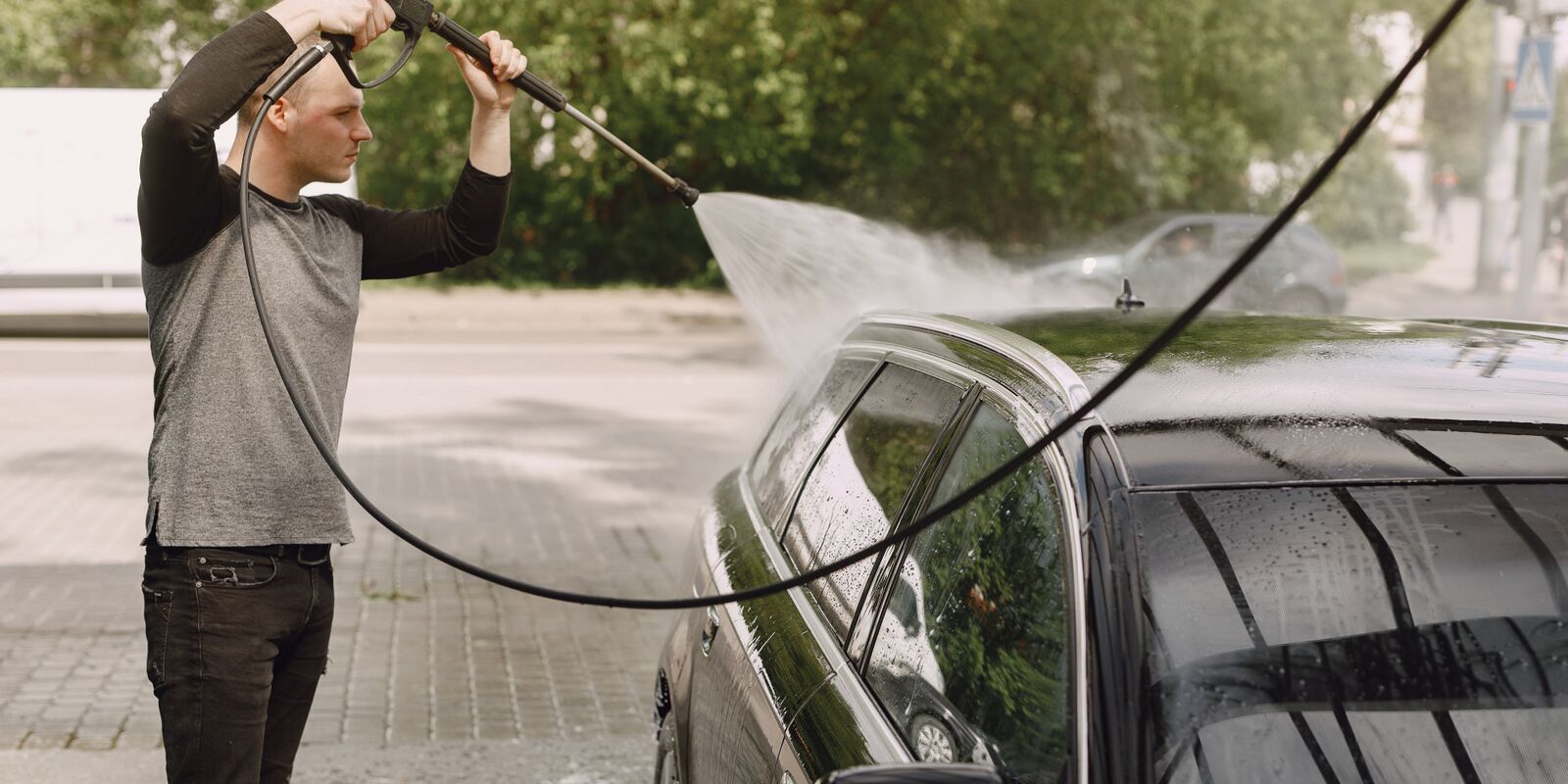 Man rinsing a dark car with a pressure washer