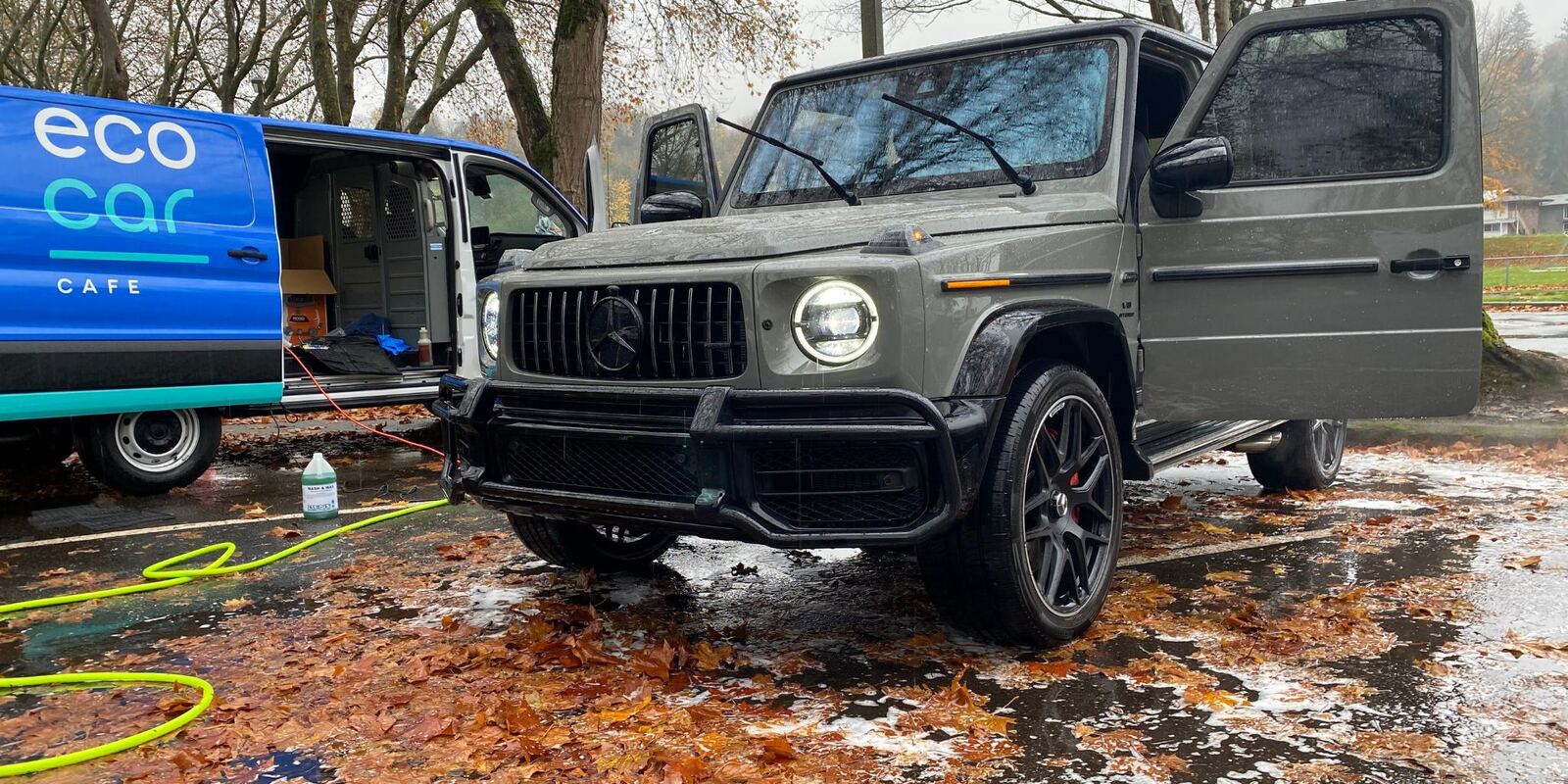 Grey Mercedes G-Class beside an Eco Car Cafe van on a leaf-covered lot