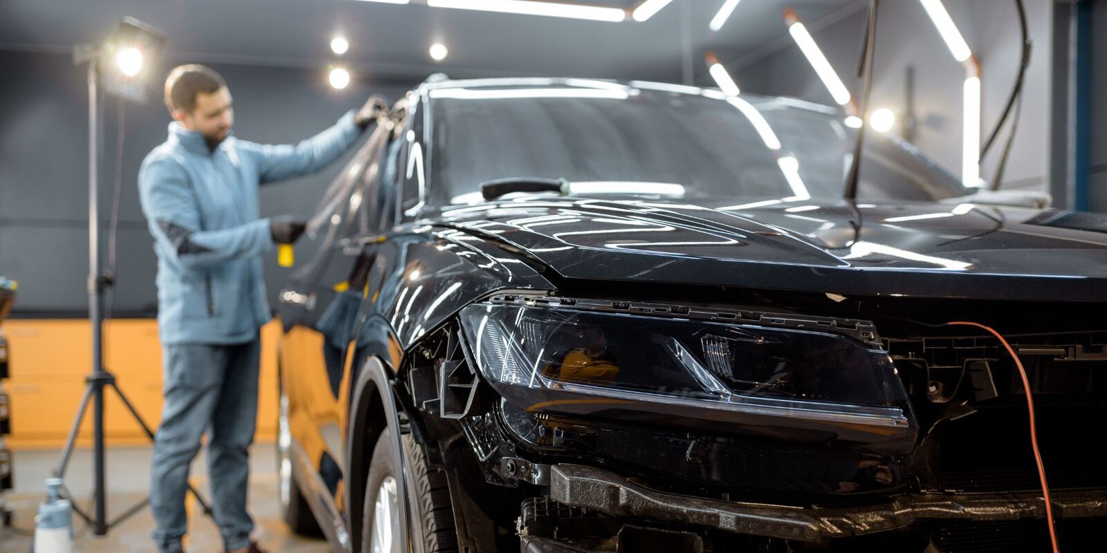 Man inspecting a black car with a damaged front end in a studio