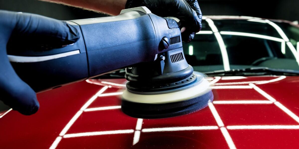 Gloved hand running a polisher over red paint