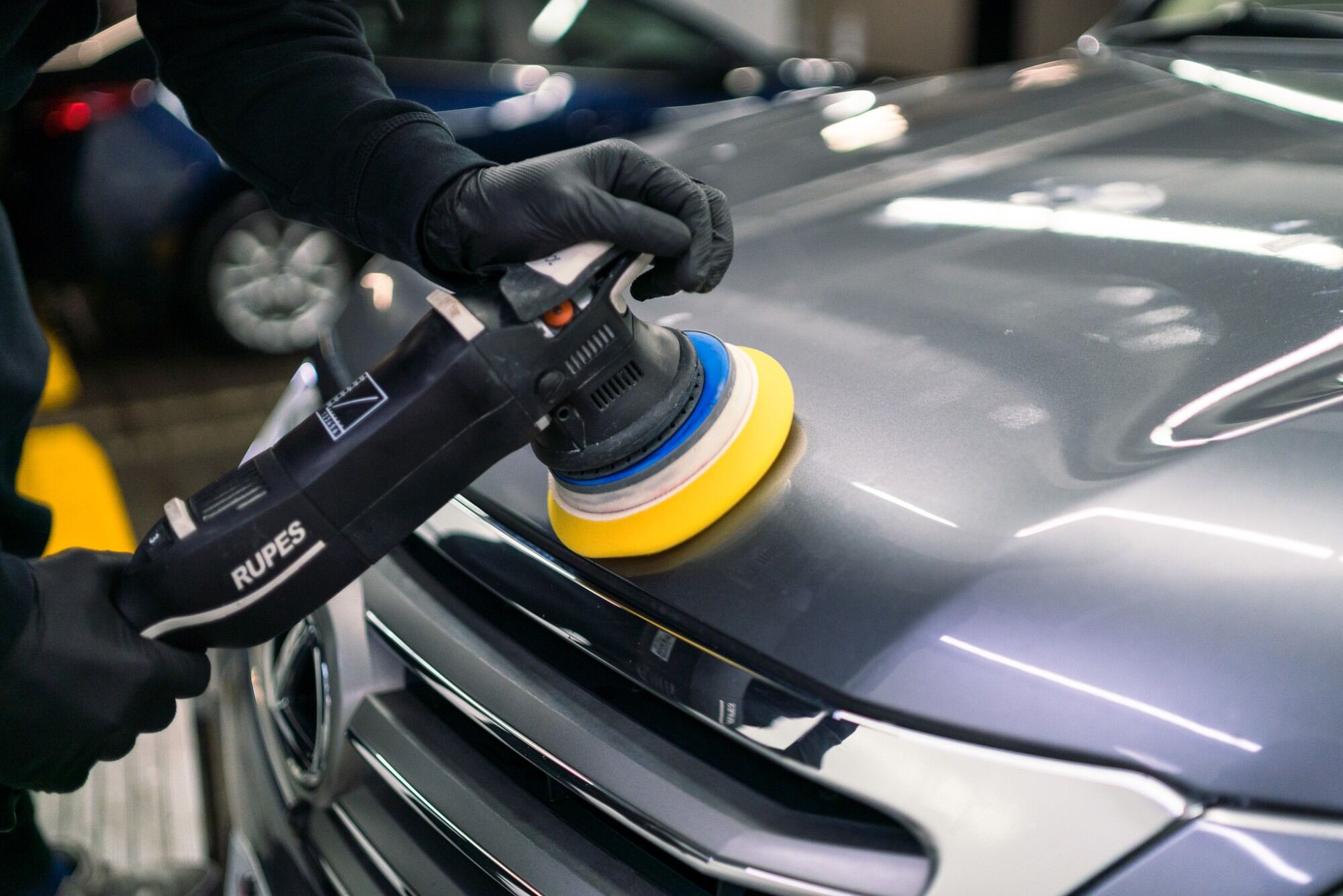 Dual-action polisher with a yellow foam pad correcting paint on a grey car hood
