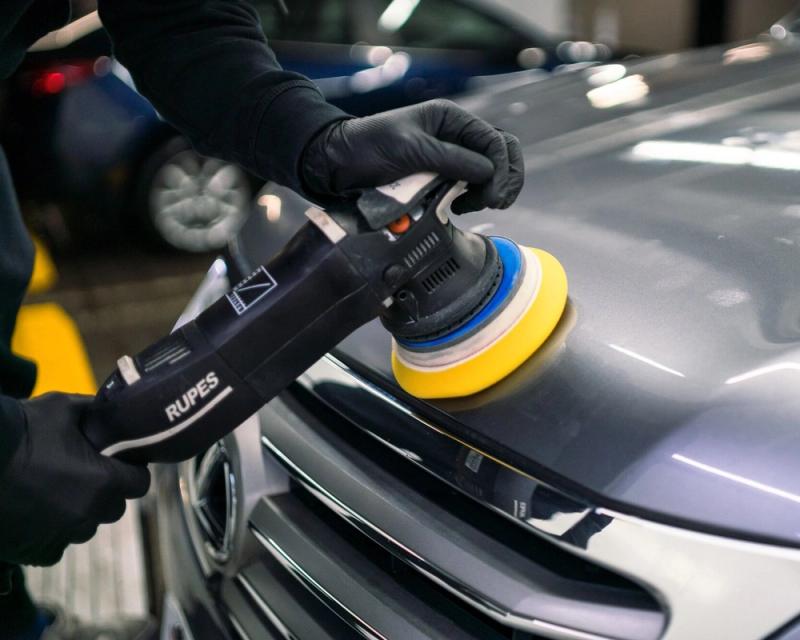 Dual-action polisher with a yellow foam pad correcting paint on a grey car hood