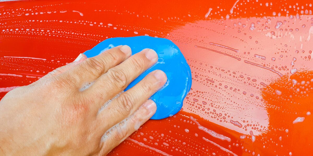 Hand pressing a blue clay bar across a wet red car panel