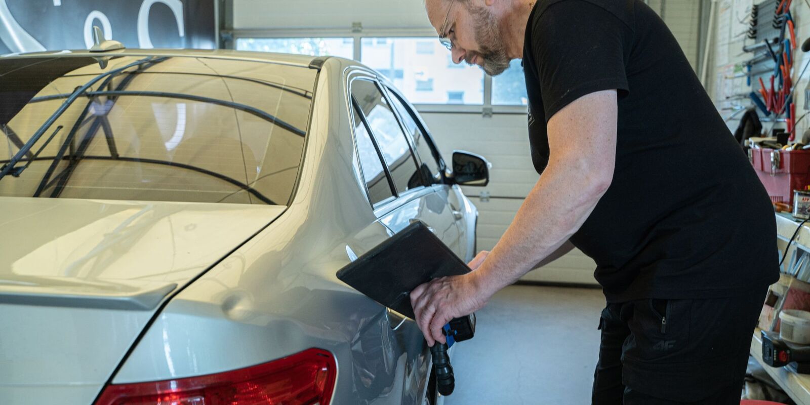 Man inspecting a silver sedan with a tablet