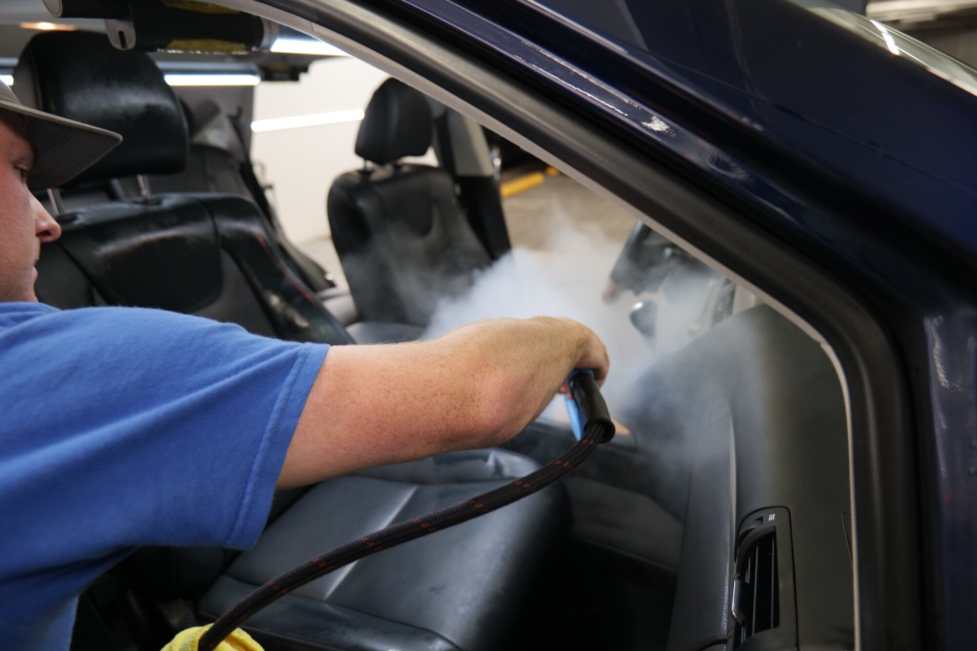 Technician steam-cleaning a leather car seat through the open driver's door