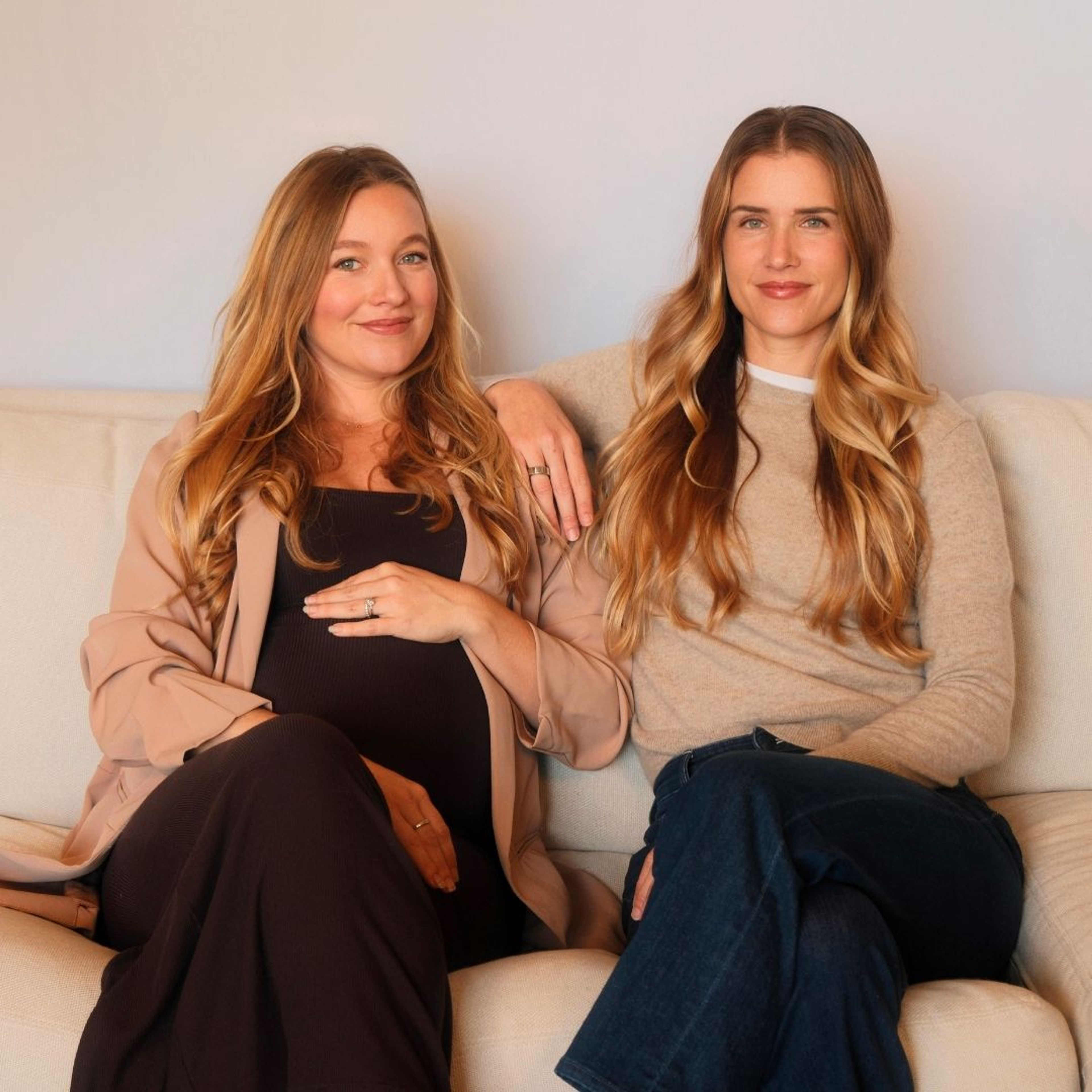 Taylor Dewey and Natasha Spaventa of Moms Interrupted Podcast seated together on a couch.